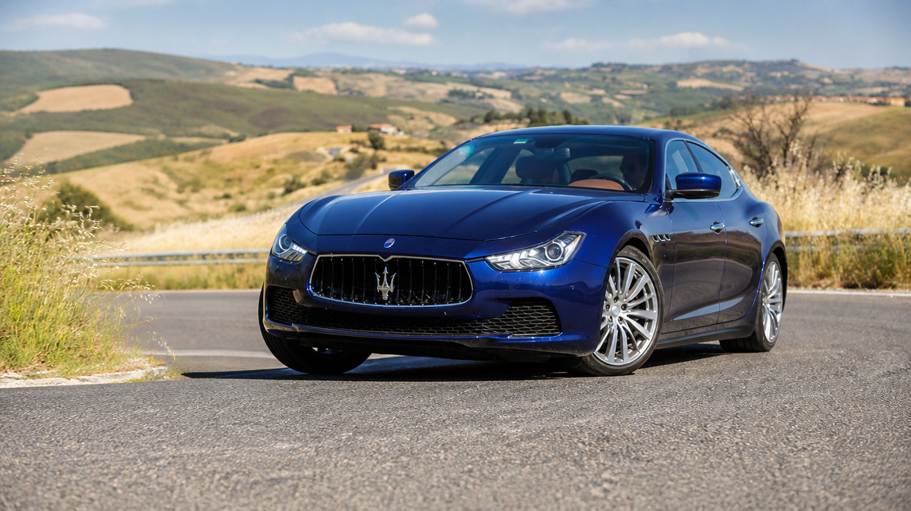 Carro esportivo azul Maserati em estrada asfaltada com paisagem rural ao fundo.