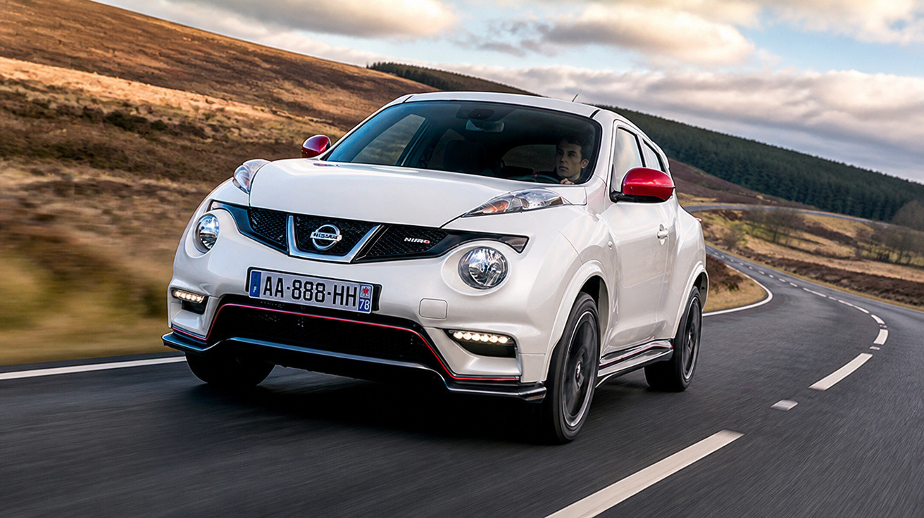 Carro branco Nissan Juke Nismo dirigindo em estrada sinuosa com detalhes vermelhos e paisagem ao fundo.