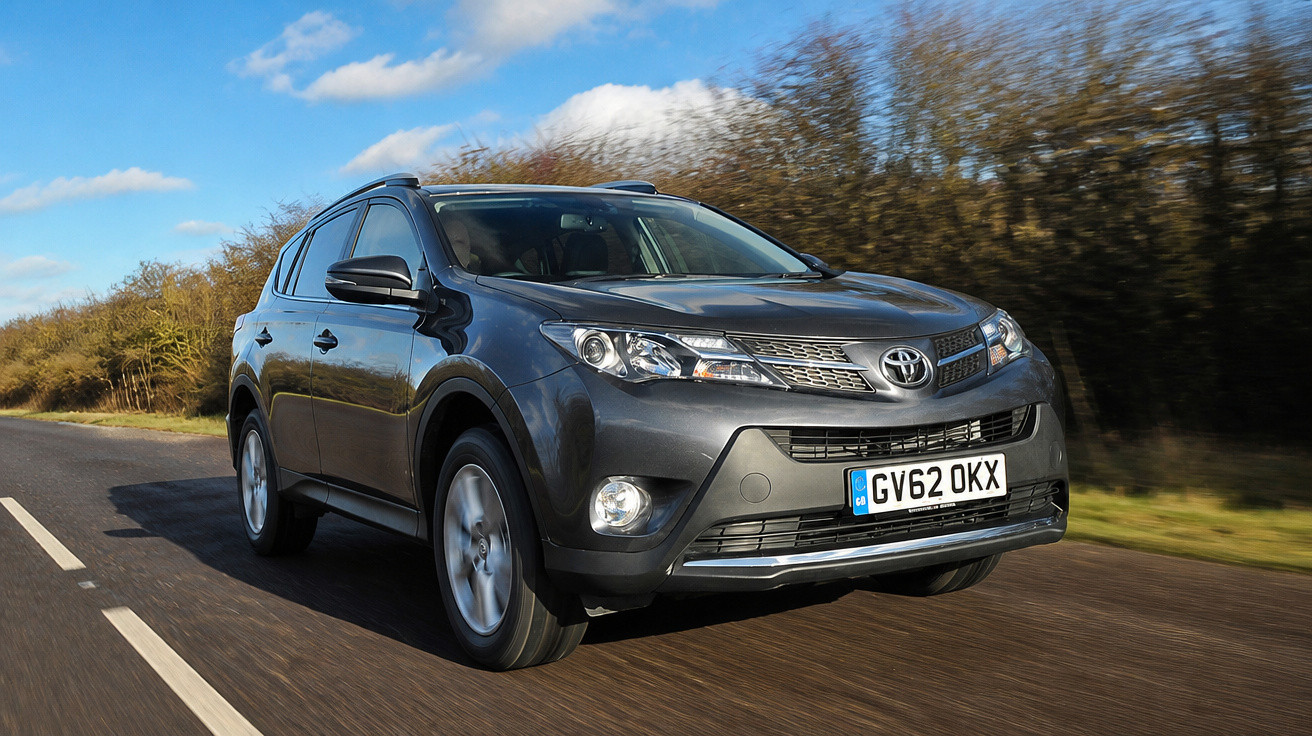 Carro SUV preto Toyota em movimento em estrada asfaltada sob céu azul com algumas nuvens.