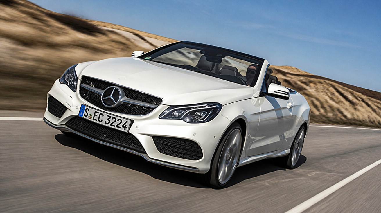 Carro conversível branco Mercedes-Benz em alta velocidade em estrada asfaltada com colinas ao fundo.