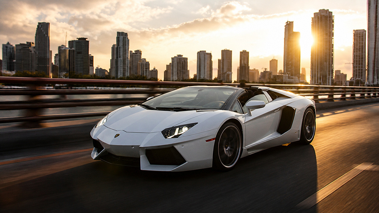 Carro esportivo branco passando em uma estrada urbana ao pôr do sol com prédios ao fundo.
