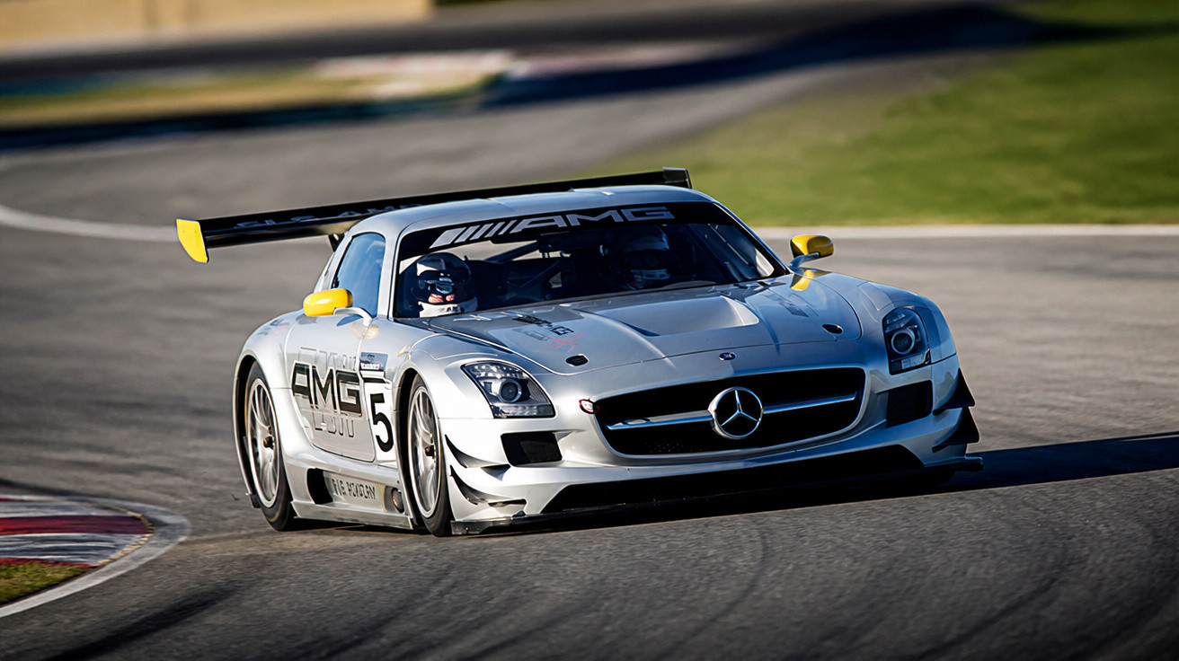 Carro de corrida Mercedes AMG prata com detalhes amarelos em pista de corrida curvada.