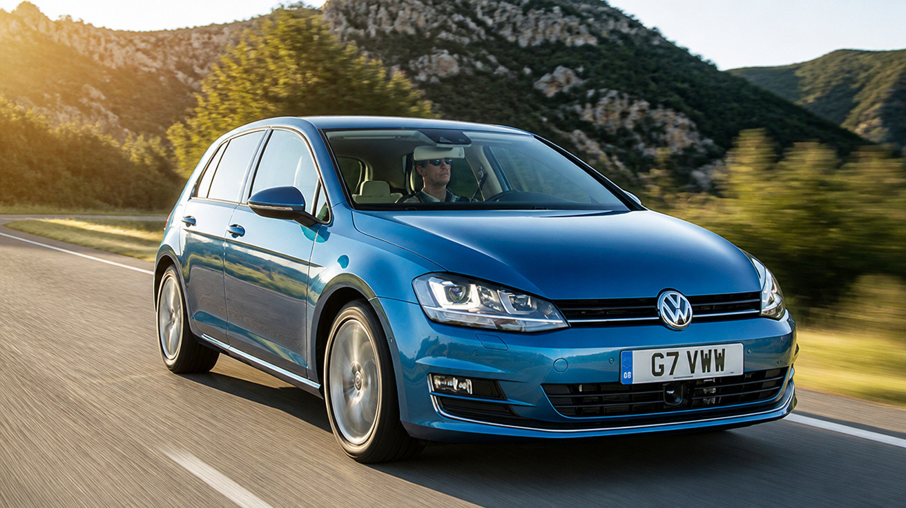 Carro Volkswagen Golf azul em estrada com motorista, paisagem de montanhas e árvores ao fundo.