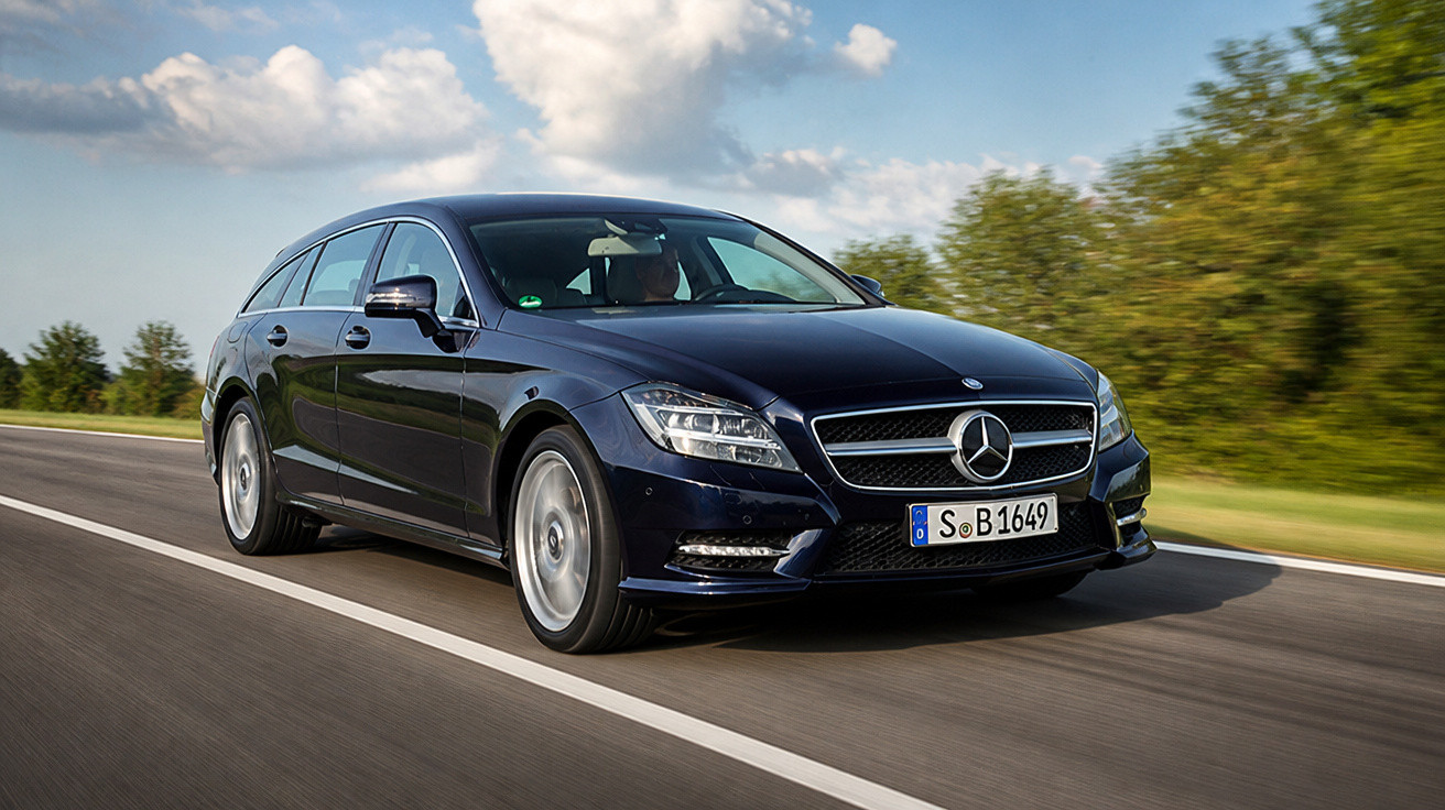 Carro Mercedes-Benz preto em movimento na estrada sob céu azul com nuvens e vegetação ao lado.