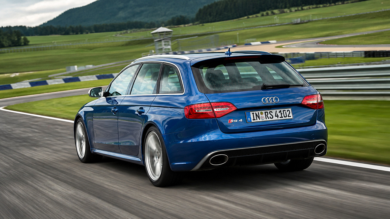 Carro Audi RS4 Avant azul em movimento em pista de corrida com paisagem verde ao fundo.