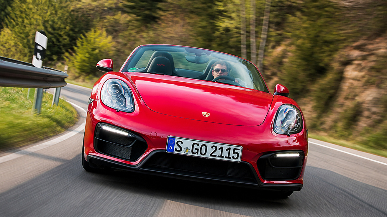 Carro esportivo conversível vermelho Porsche dirigido em estrada sinuosa cercada por vegetação.