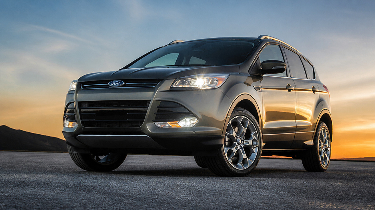 SUV Ford cinza estacionado em estrada ao pôr do sol com luzes dianteiras acesas.