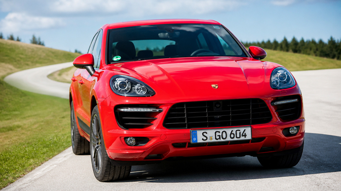 Carro SUV esportivo vermelho estacionado em estrada curva, com paisagem verde e céu azul ao fundo.