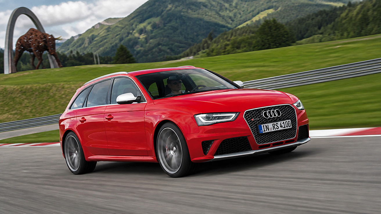 Carro Audi RS vermelho em curva de pista com montanhas verdes ao fundo e escultura de leopardo.