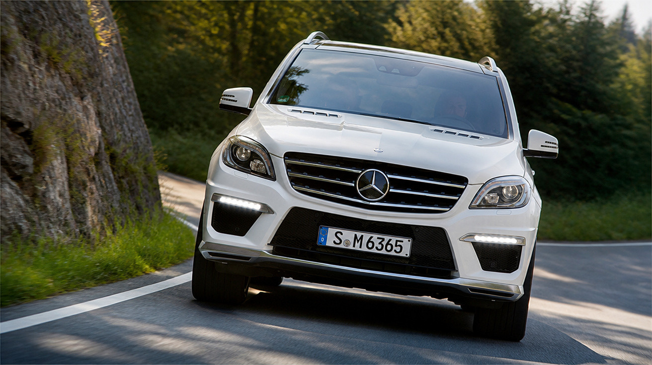 Carro SUV Mercedes-Benz branco em curva de estrada rodeada por árvores e rochas.