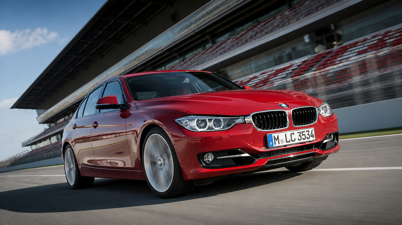 Carro BMW sedan vermelho em alta velocidade na pista de corrida com arquibancada ao fundo.