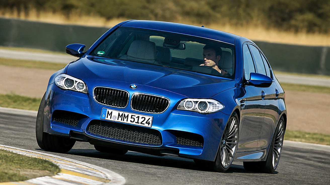 Carro BMW azul em curva acentuada em pista com motorista ao volante.