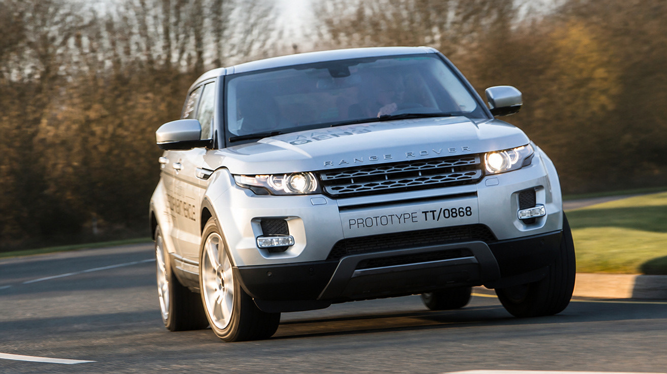 SUV Range Rover prata em estrada pavimentada com fundo de árvores e luz do entardecer.