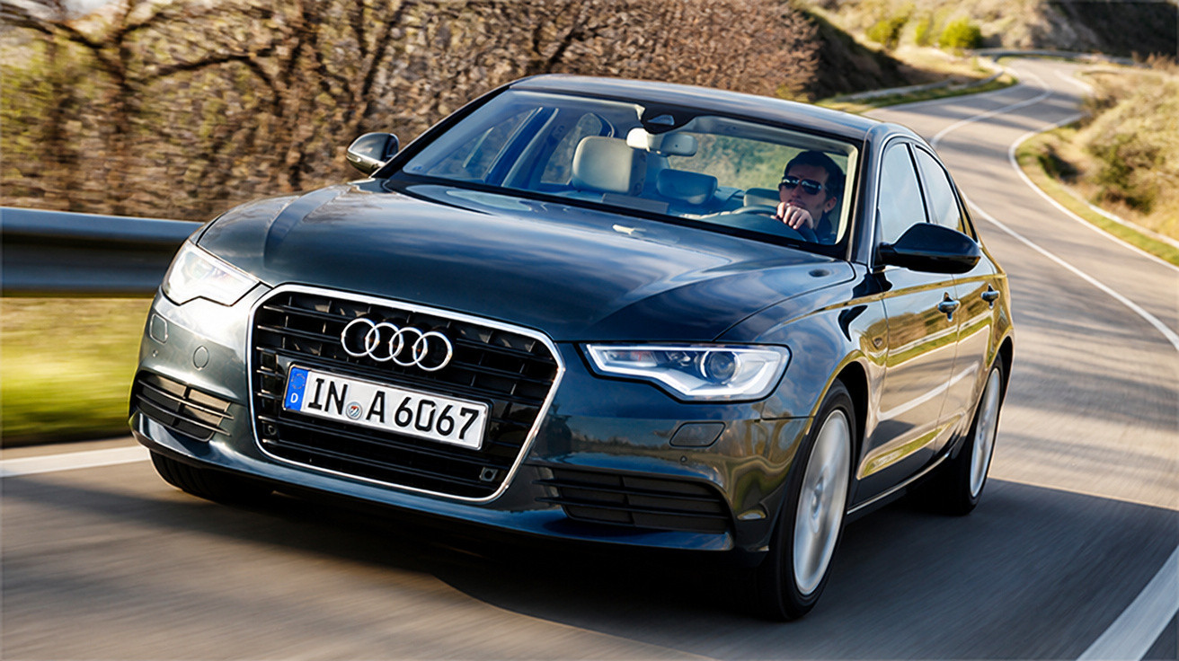 Carro preto Audi A6 dirigindo em estrada sinuosa com motorista usando óculos escuros.