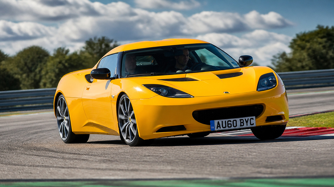 Carro esportivo amarelo em curva em pista de corrida com céu nublado ao fundo.