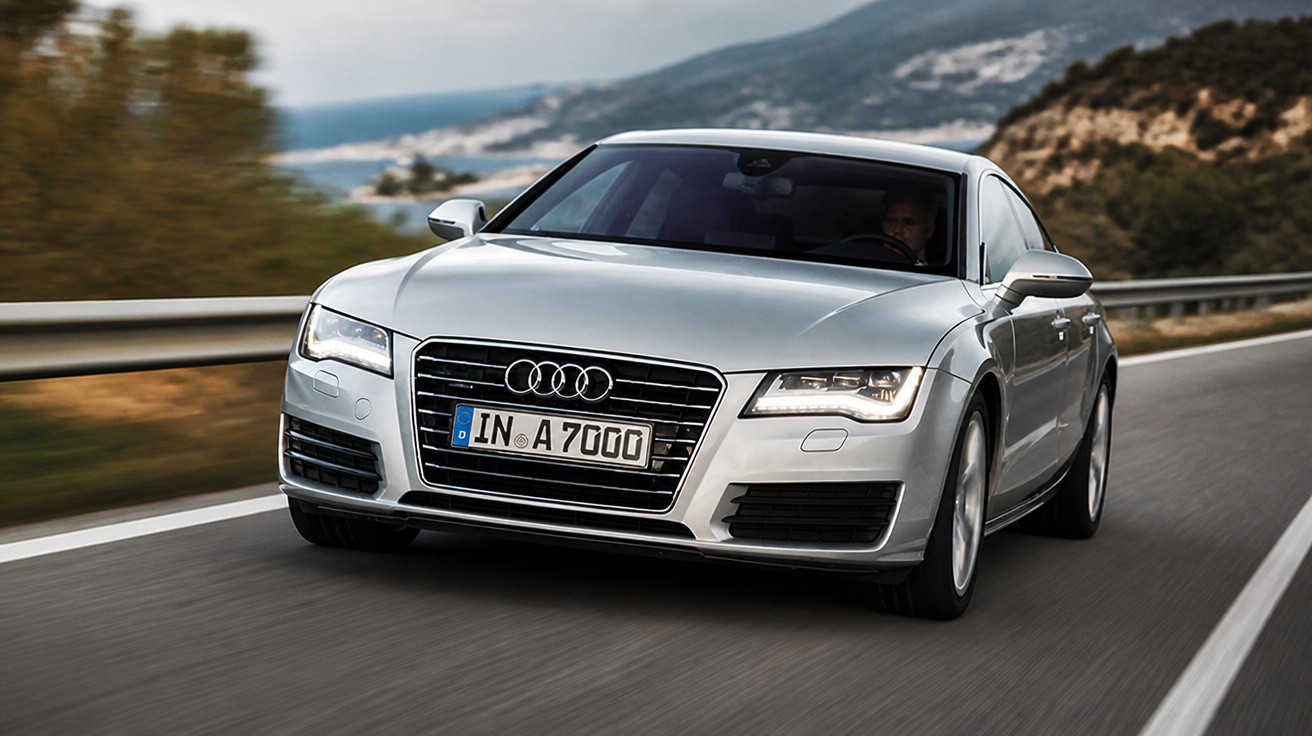 Carro Audi prata em movimento veloz em estrada sinuosa com montanhas ao fundo.