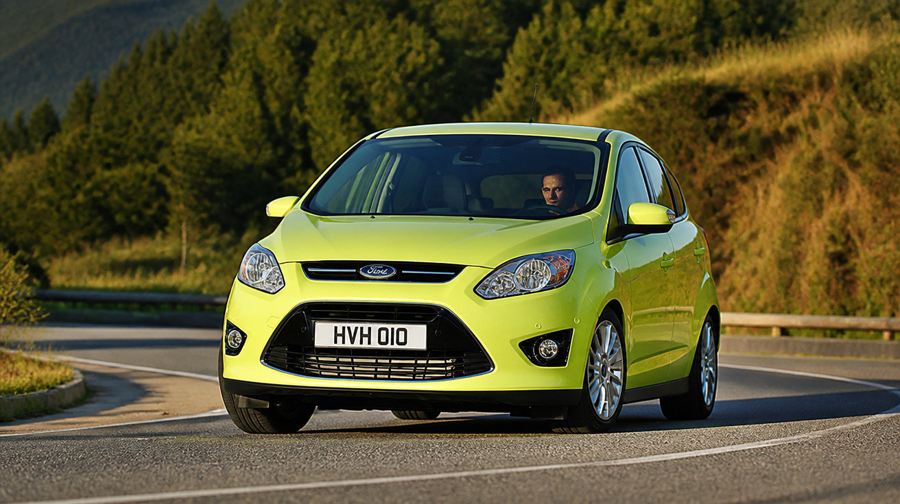 Carro Ford amarelo dirigindo em estrada curva com paisagem de árvores ao fundo.