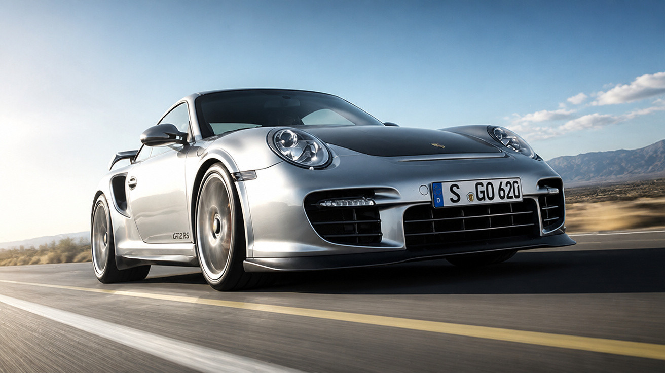 Carro esportivo Porsche 911 GT2 RS prata em alta velocidade numa estrada com céu azul e montanhas ao fundo.