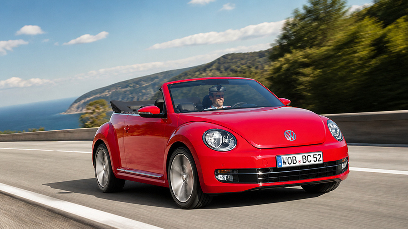 Carro conversível vermelho modelo Volkswagen Beetle sendo dirigido em estrada costeira.