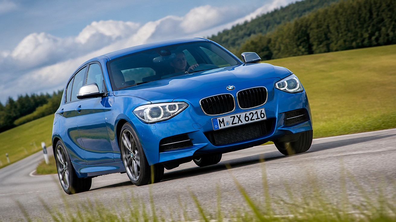 Carro azul BMW dirigindo em estrada rural com paisagem verde e céu azul nublado.