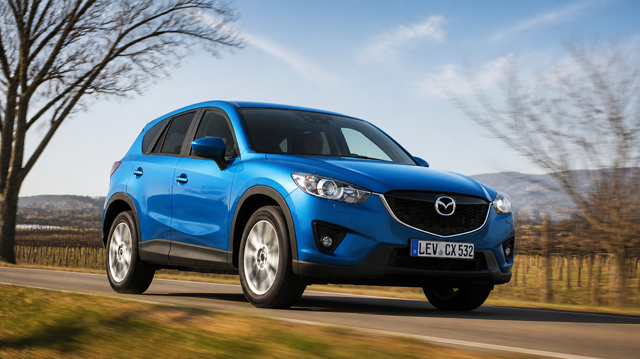 Carro SUV azul Mazda em estrada rural com árvores e céu claro ao fundo.