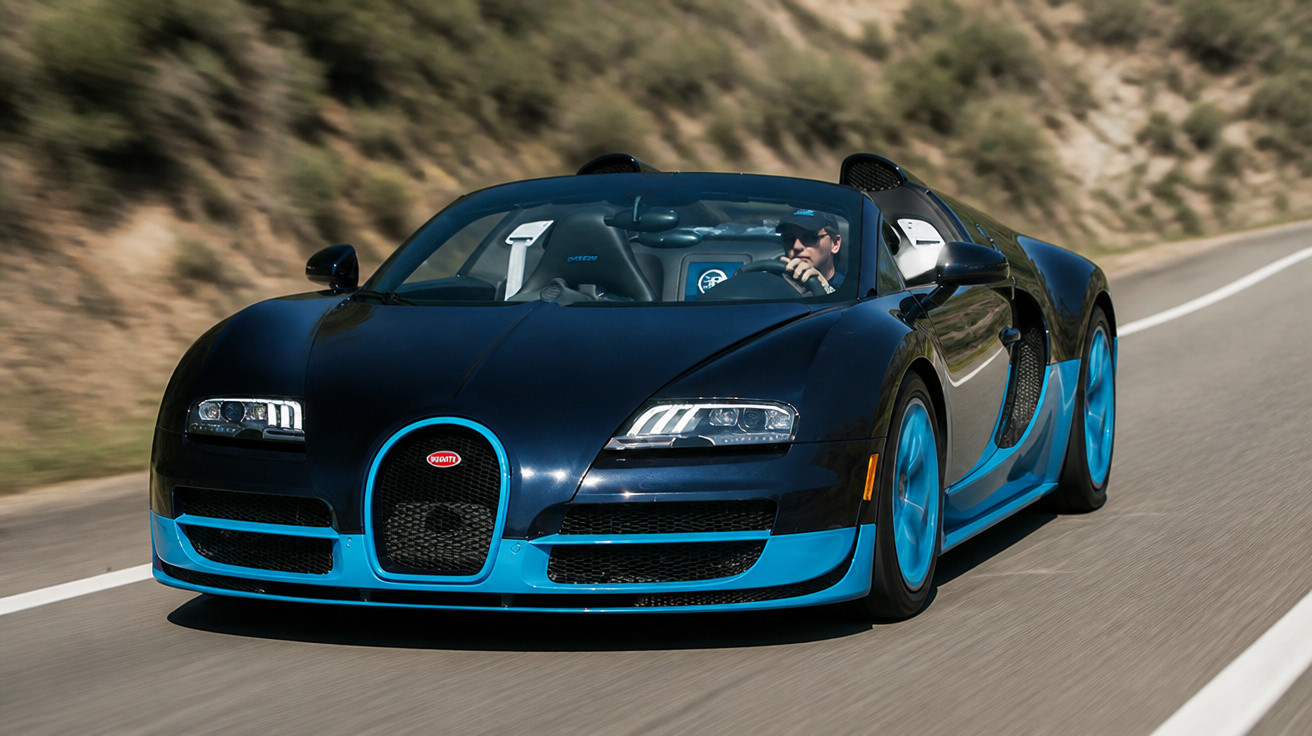 Carro esportivo preto e azul Bugatti Veyron dirigindo em estrada sinuosa com motorista usando óculos escuros.