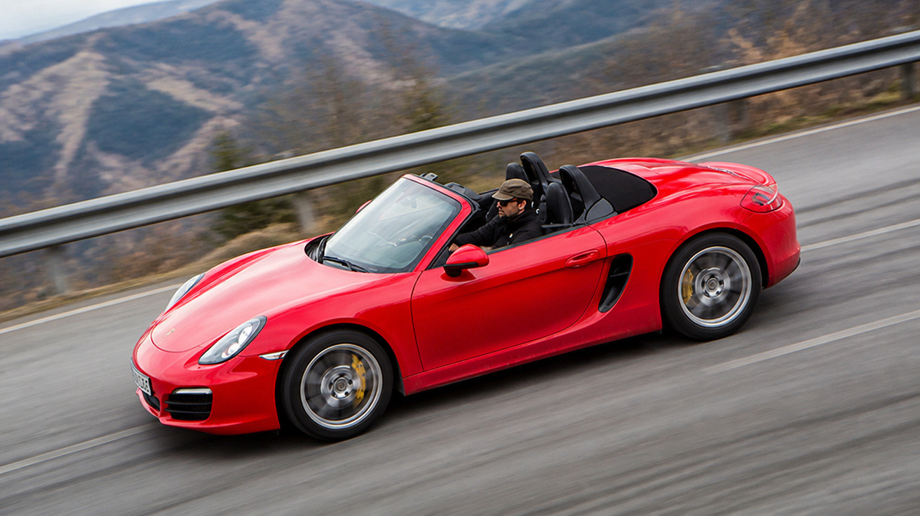 Carro esportivo conversível vermelho com motorista usando boné em estrada de montanha.