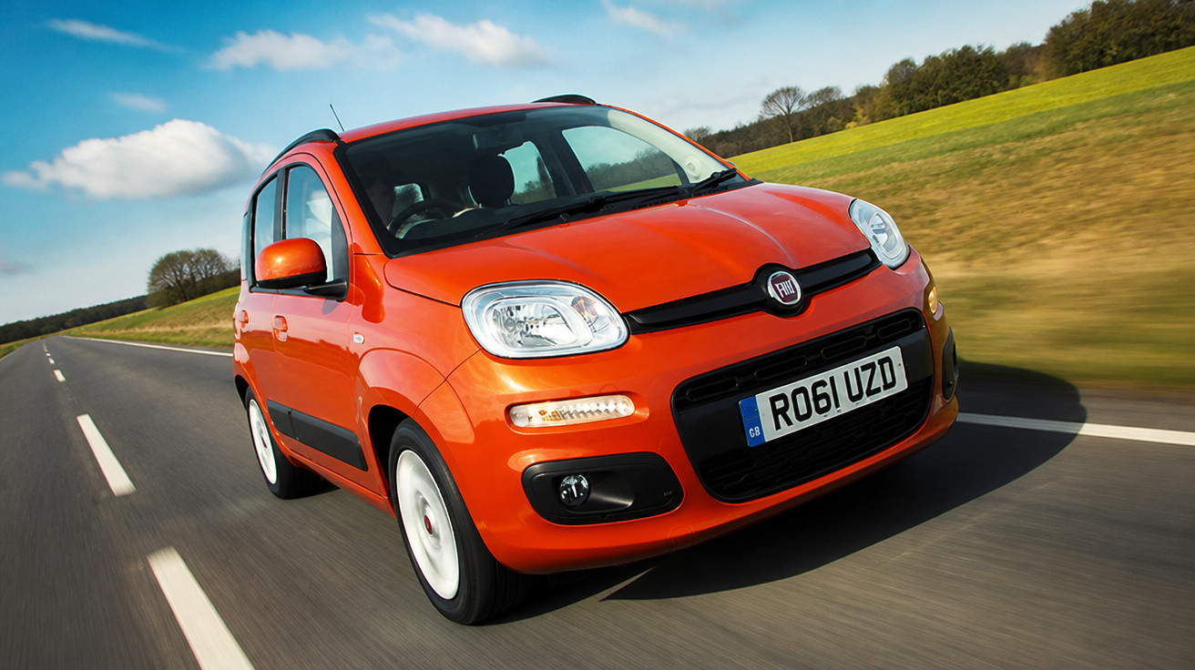 Carro Fiat Punto laranja em movimento em estrada asfaltada com campos ao fundo.