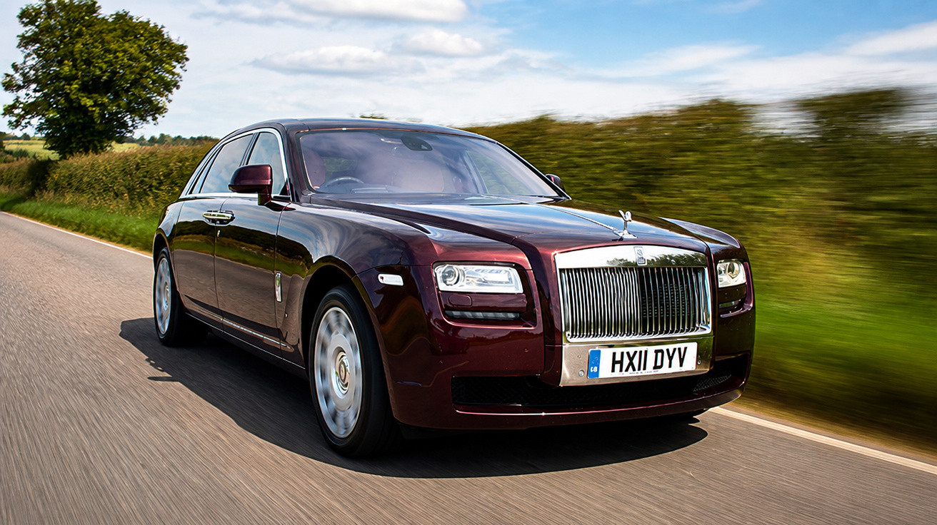 Carro de luxo Rolls-Royce preto em estrada rural sob céu parcialmente nublado.