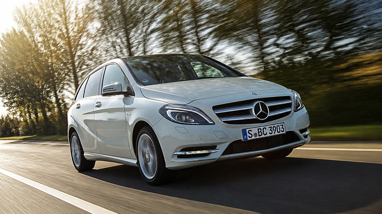 Carro branco Mercedes-Benz em movimento em estrada com árvores ao fundo em dia ensolarado.