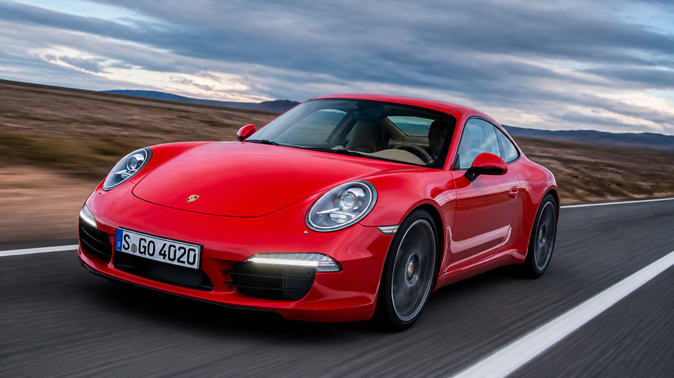 Carro esportivo vermelho Porsche 911 dirigido em estrada reta com céu nublado ao fundo.
