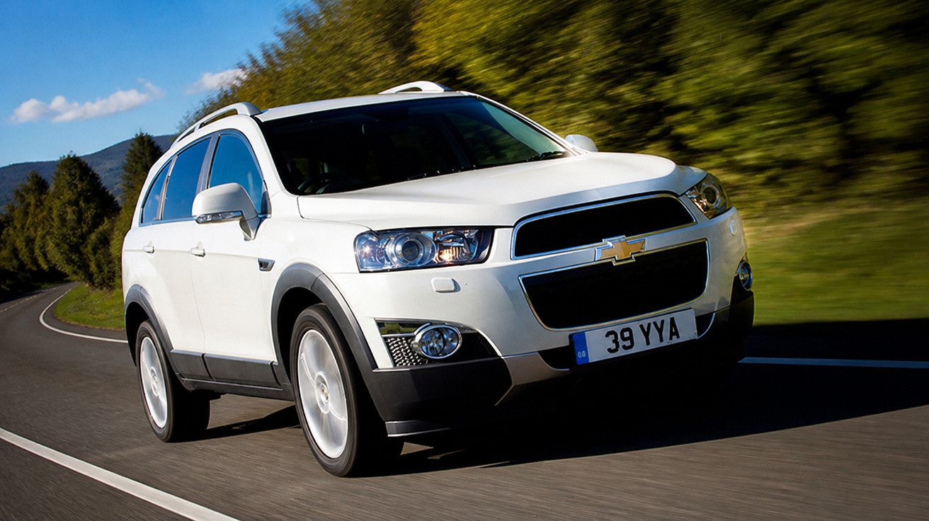 Carro SUV branco da Chevrolet em movimento numa estrada cercada por árvores verdes.