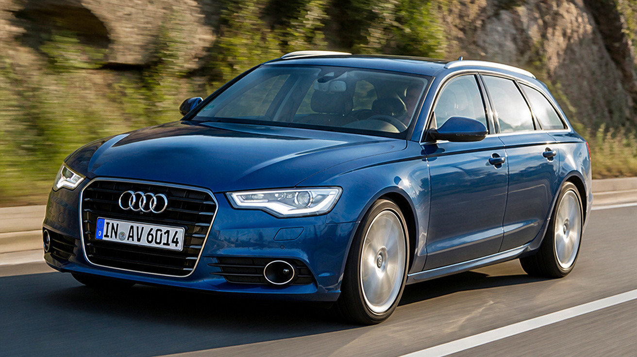 Carro Audi azul metálico modelo perua em movimento em estrada asfaltada com pedras ao fundo.