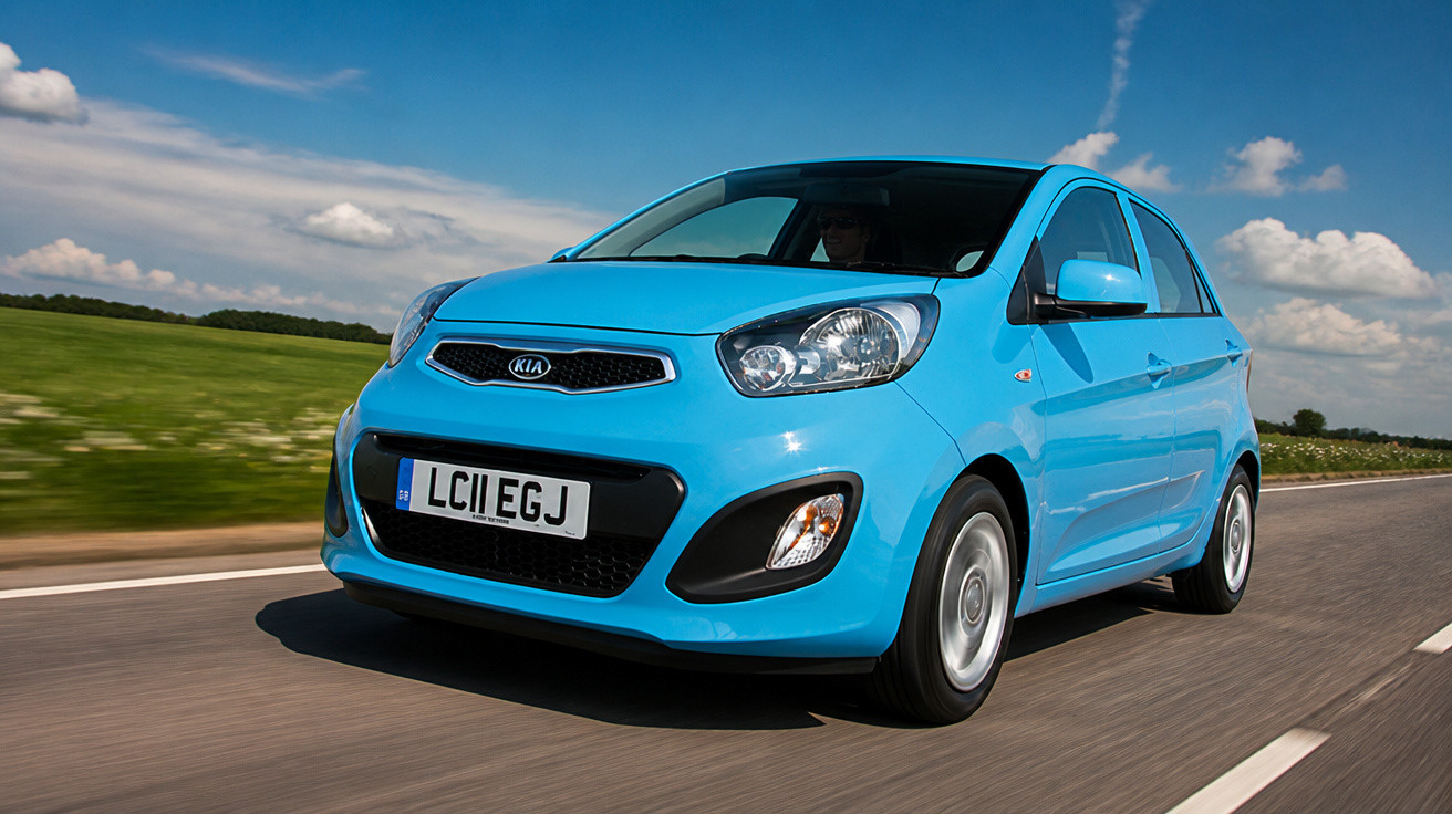 Carro azul Kia compacto em movimento em estrada com céu azul e campo ao fundo.