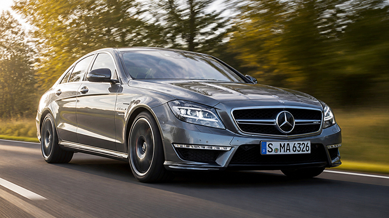 Carro Mercedes-Benz cinza em movimento numa estrada rodeada por árvores desfocadas.