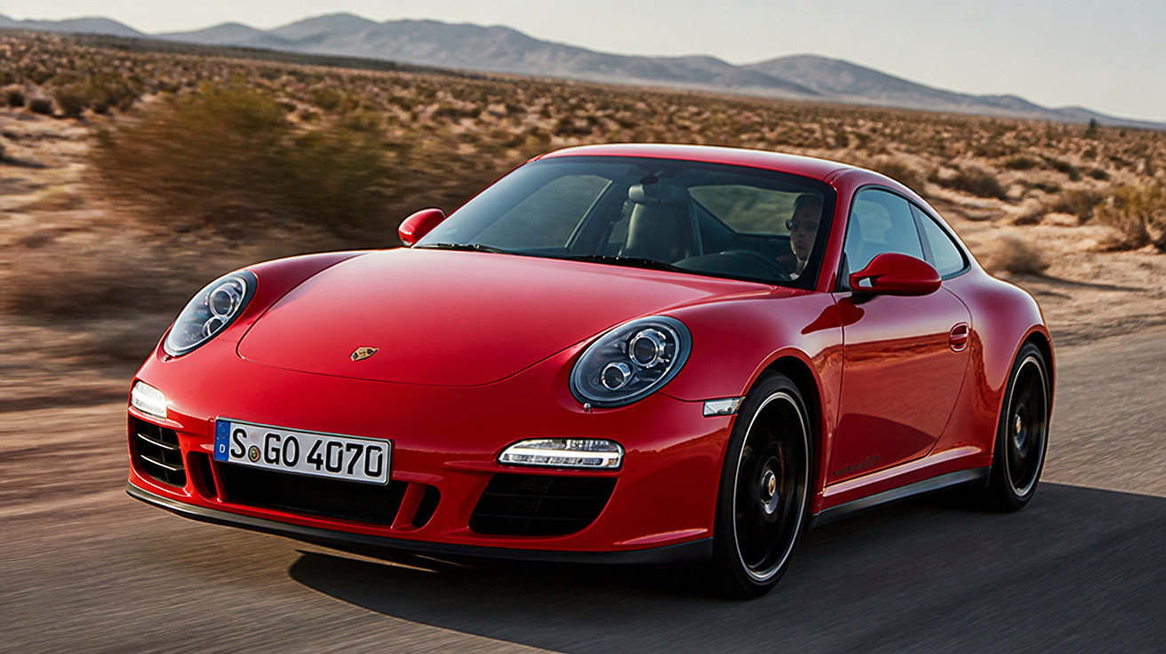 Carro esportivo Porsche vermelho dirigido em estrada deserta com montanhas ao fundo.