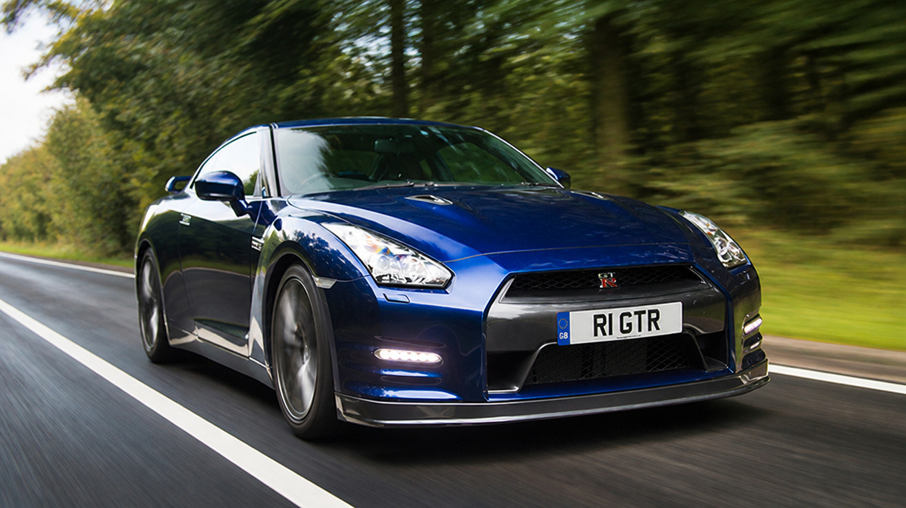 Carro esportivo azul Nissan GT-R em alta velocidade em rodovia cercada por árvores.