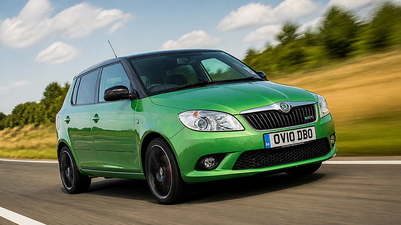 Carro hatchback verde em movimento em estradas com paisagem natural ao fundo em dia ensolarado.