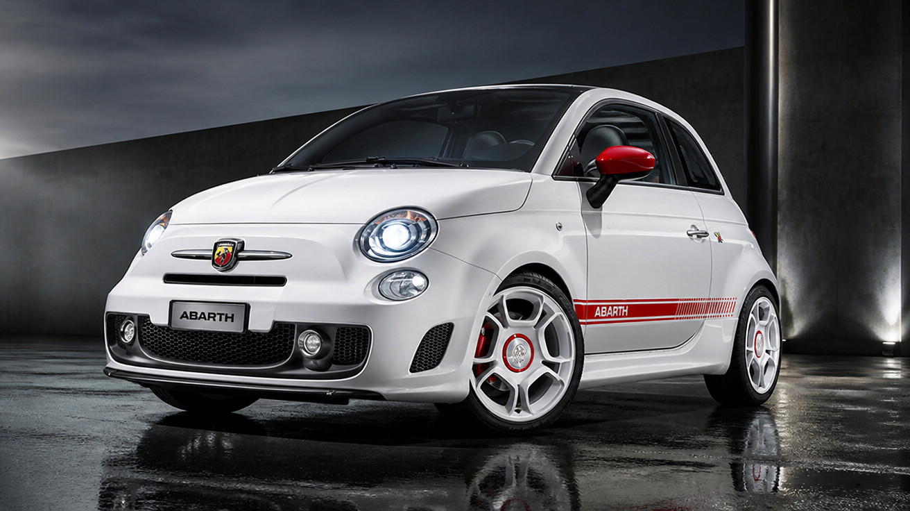 Carro esportivo Fiat 500 Abarth branco com detalhes vermelhos estacionado em piso molhado.