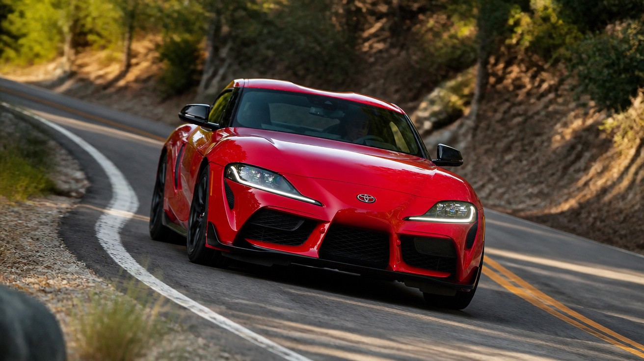 Carro esportivo vermelho Toyota Supra em curva de estrada cercada por árvores e vegetação.