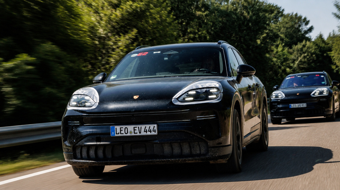 Dois carros SUV pretos Porsche em estrada cercada de árvores, em movimento, focados no primeiro veículo.
