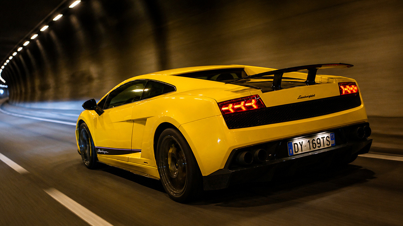 Carro esportivo amarelo Lamborghini trafegando em túnel iluminado durante a noite.