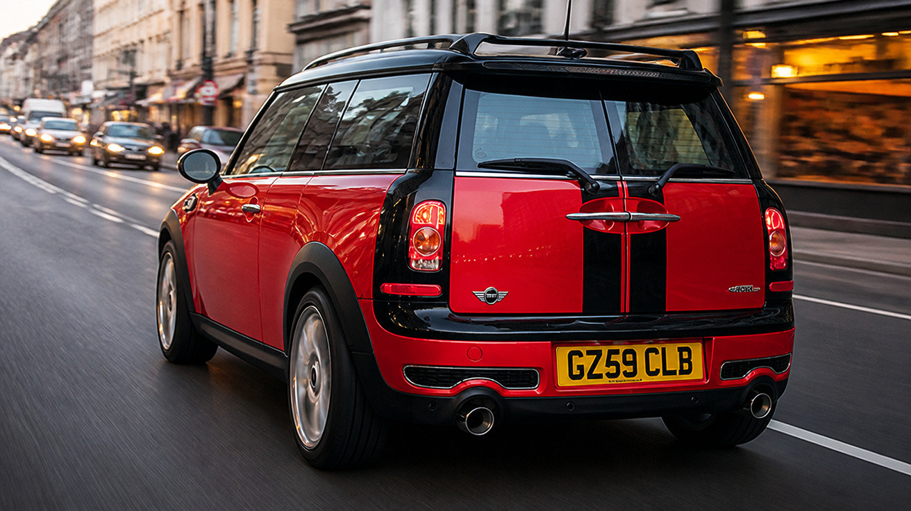 Carro Mini Cooper vermelho com faixas pretas trafegando por rua movimentada na cidade.