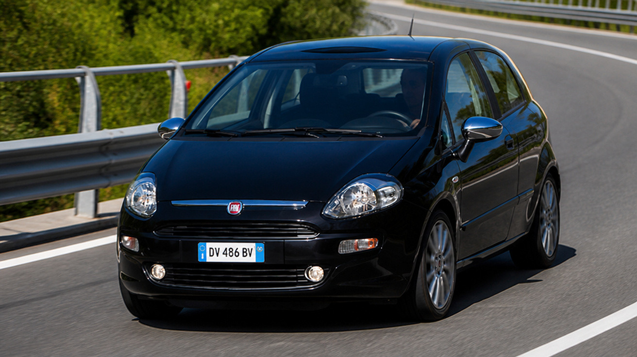 Carro preto Fiat Punto em curva de estrada asfaltada com proteção metálica e vegetação ao fundo.