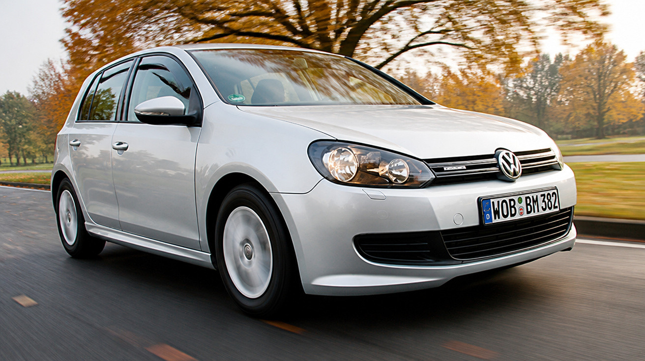 Carro Volkswagen prata modelo hatchback em movimento em estrada com árvores ao fundo no outono.