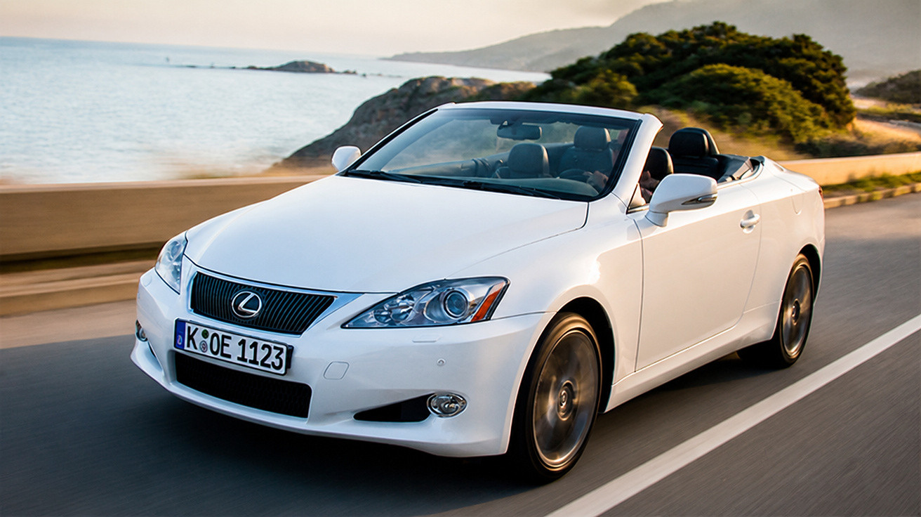 Carro conversível branco Lexus em uma estrada à beira-mar com colinas ao fundo e céu ao entardecer.