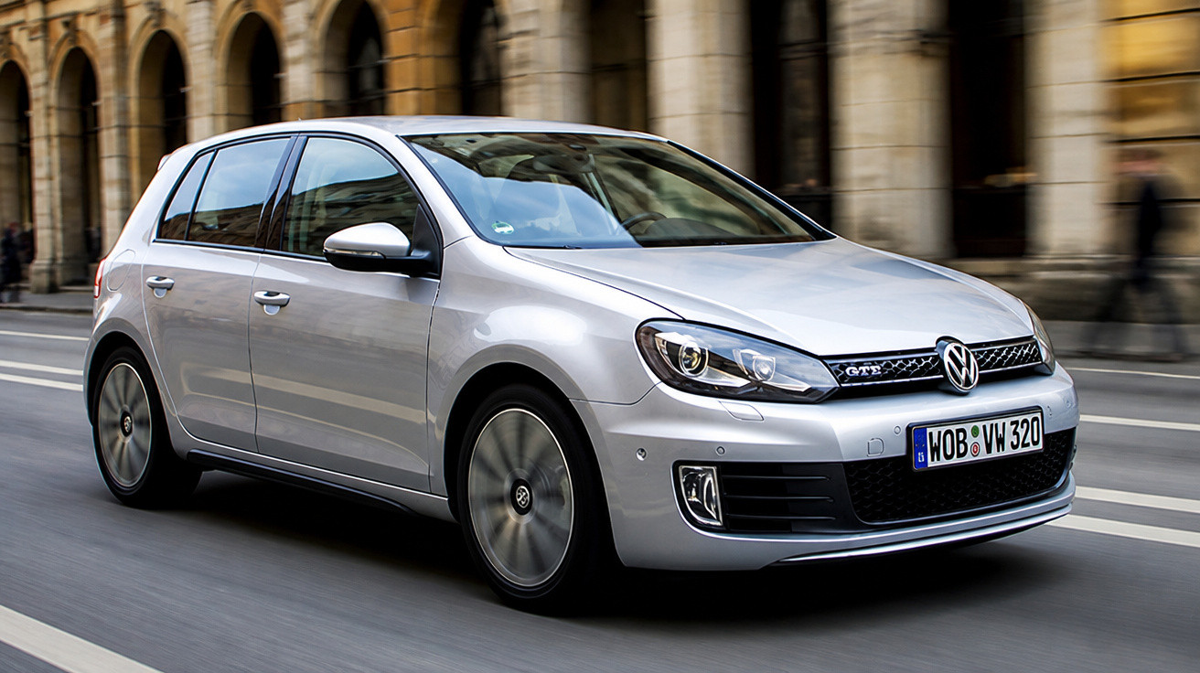 Carro Volkswagen Golf cinza prata em movimento em rua com edifício antigo ao fundo.