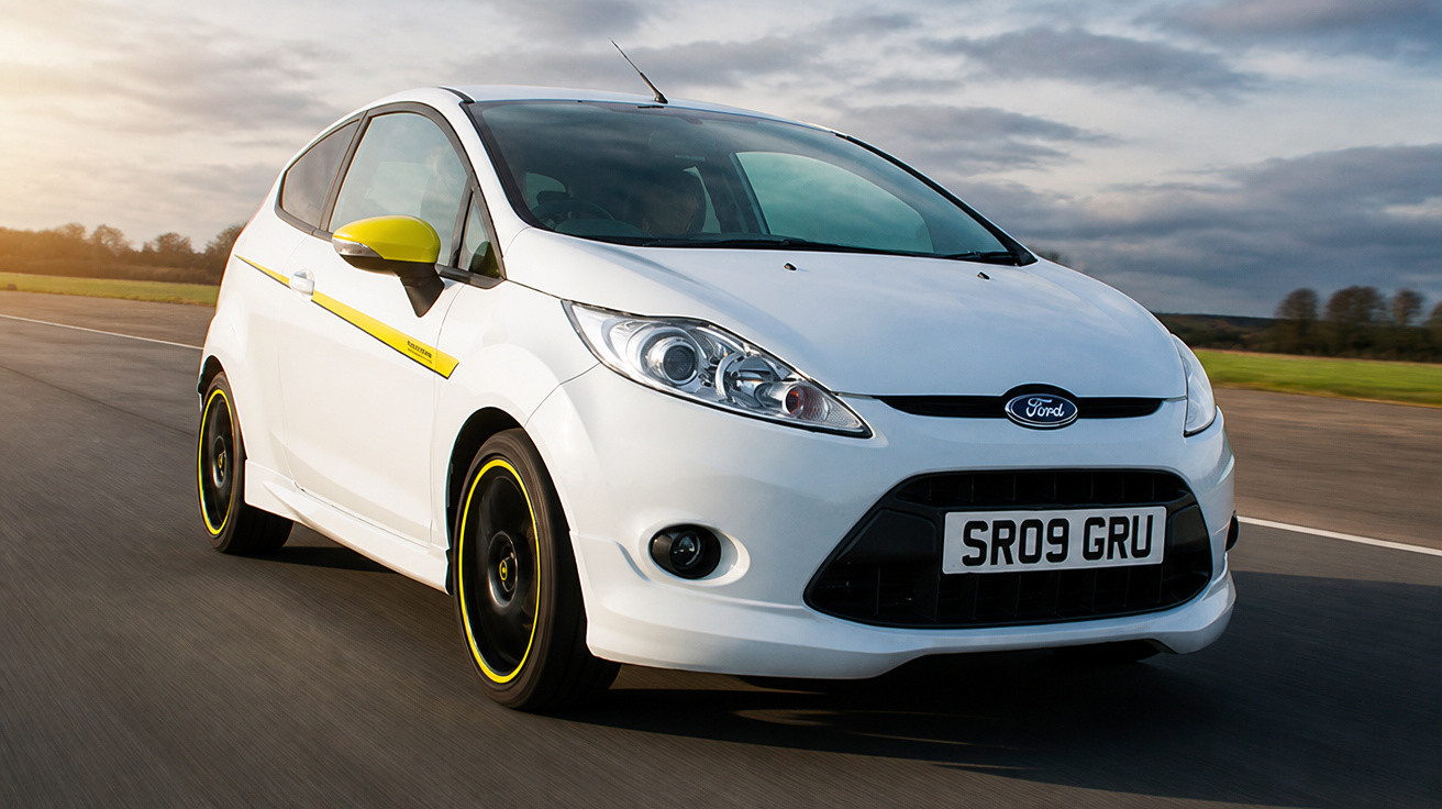 Carro branco Ford Fiesta em movimento em estrada com detalhes amarelos nas rodas e retrovisor.
