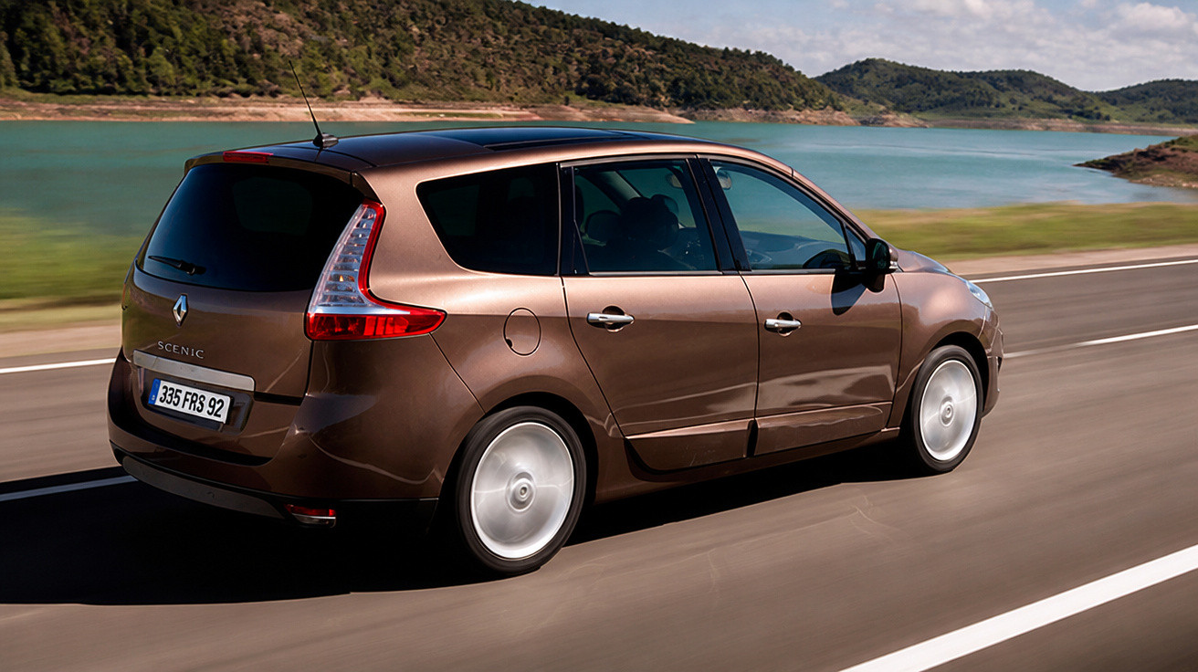 Carro Renault Scenic marrom em movimento numa estrada próxima a um lago e montanhas.