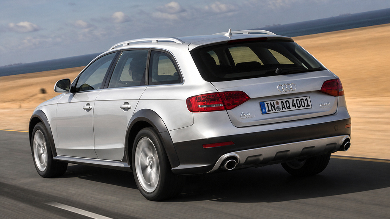 Carro Audi A4 Avant cinza em movimento na estrada, com paisagem de campo ao fundo.